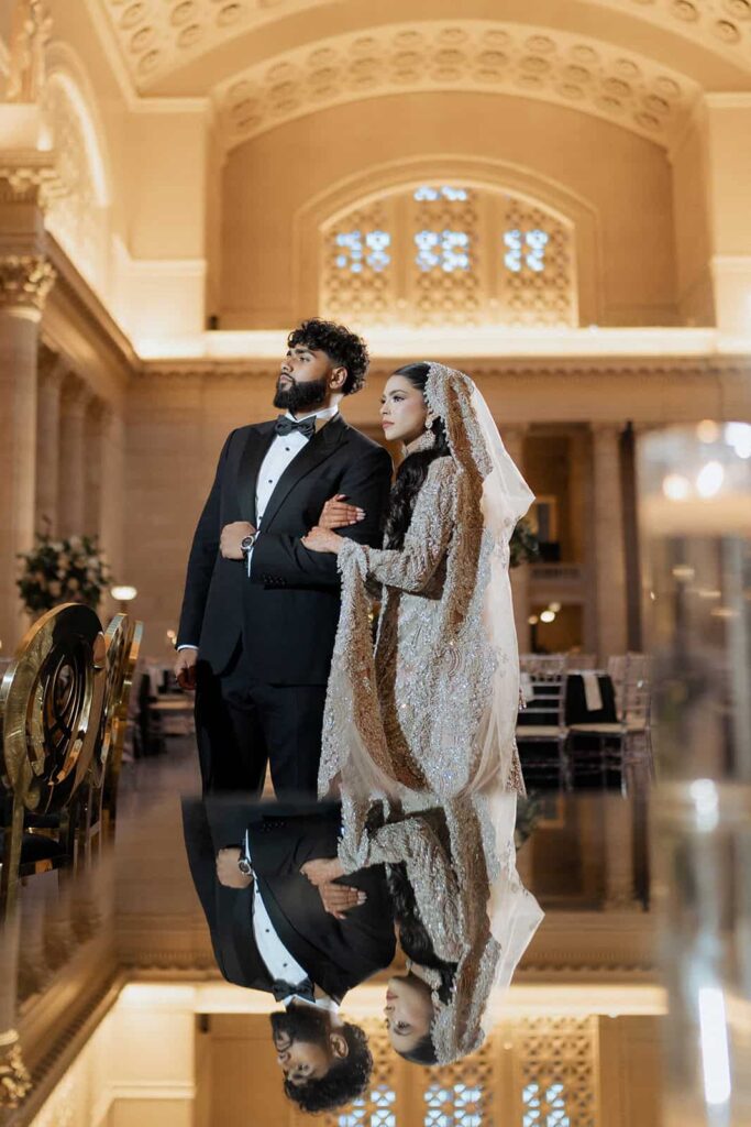 Elegant couple in wedding attire in a luxurious high-end venue with ornate architecture and warm lighting.