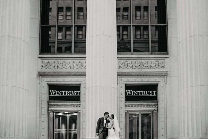 Elegant black and white wedding photo of a bride and groom in front of a historic building with ornate architectural details. Perfect for luxury wedding venues.