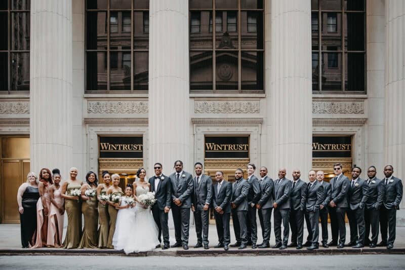 Elegant wedding party posing outside a historic high-end building, showcasing luxury wedding photography.
