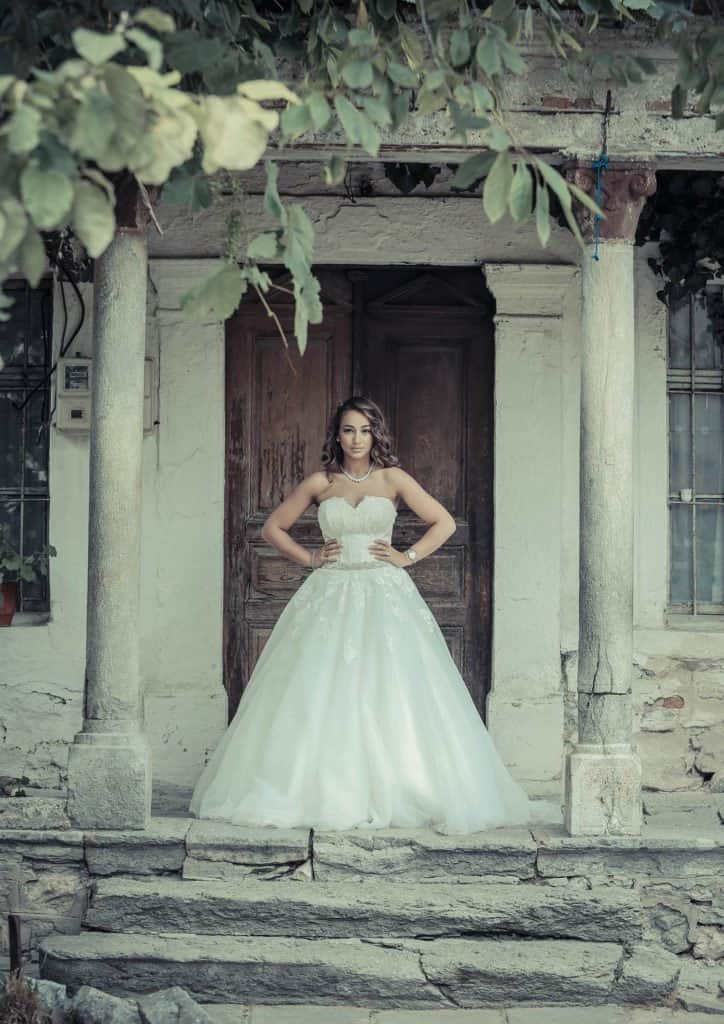 Elegant bride in a white wedding gown standing on rustic stone steps in front of an old house at a luxury wedding venue.