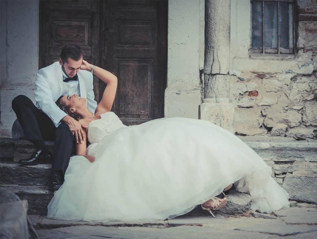 Elegant wedding couple sharing a romantic moment outdoors in front of rustic stone walls, showcasing timeless luxury and romance.