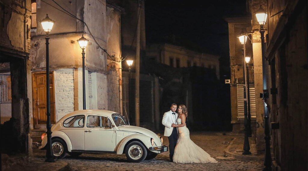 Vintage wedding couple on romantic night street with classic car, high-end luxury wedding, stylish ambiance, elegant venue, nighttime cityscape.