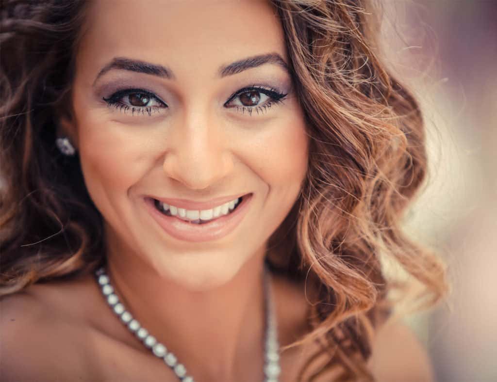Luxury bride portrait at high-end wedding venue with elegant jewelry and makeup, outdoor setting.