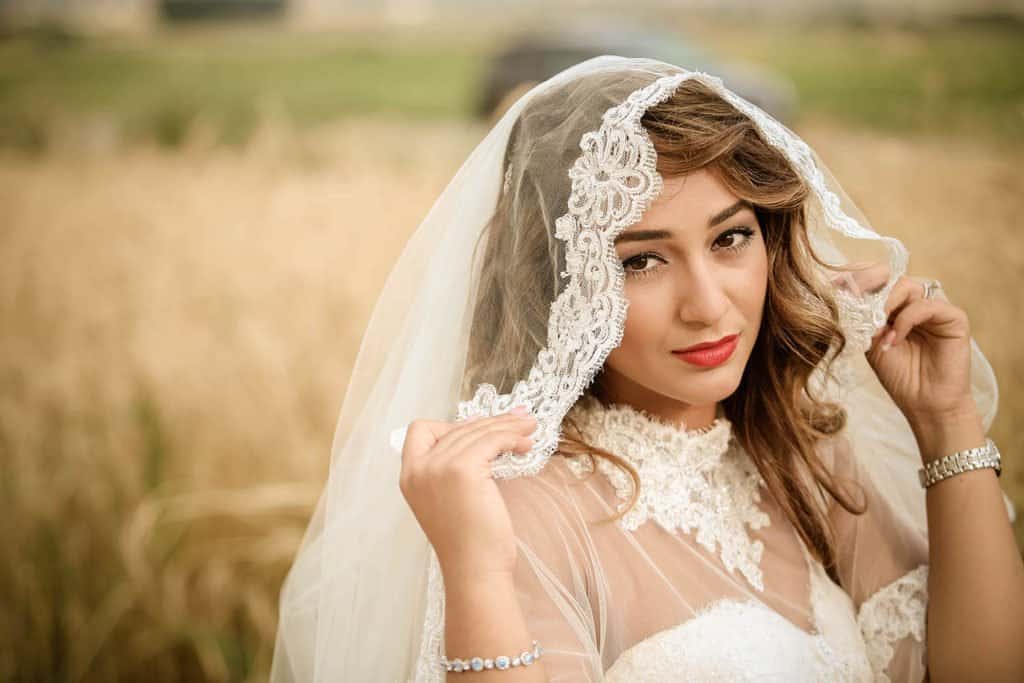 Luxury bridal portrait in a natural outdoor setting, elegant wedding dress with lace veil, high-end wedding photography, timeless beauty, scenic countryside backdrop.