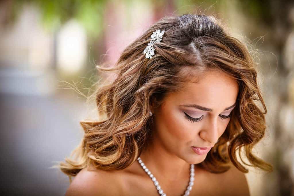Elegant bride with wavy hair and floral hair accessory at luxury outdoor wedding venue.