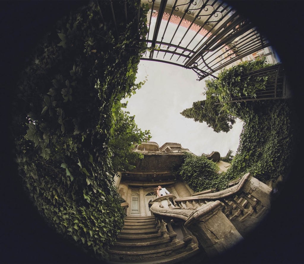 Elegant couple on historic outdoor staircase at luxury wedding venue with lush greenery.