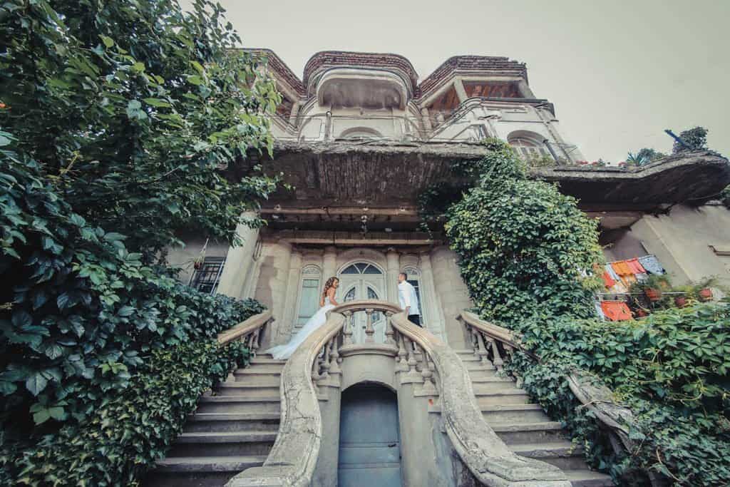Elegant couple on historic mansion staircase for luxury wedding photoshoot.