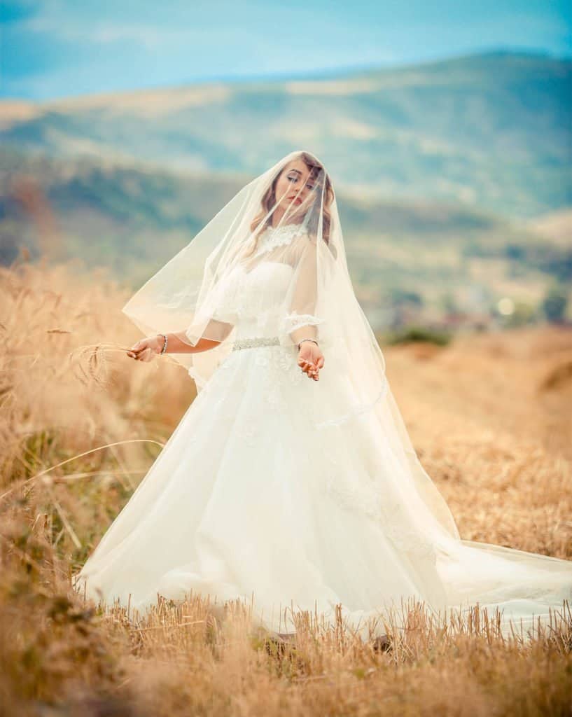 Elegant bride in a wedding gown with veil outdoors in natural landscape for luxury wedding photos.