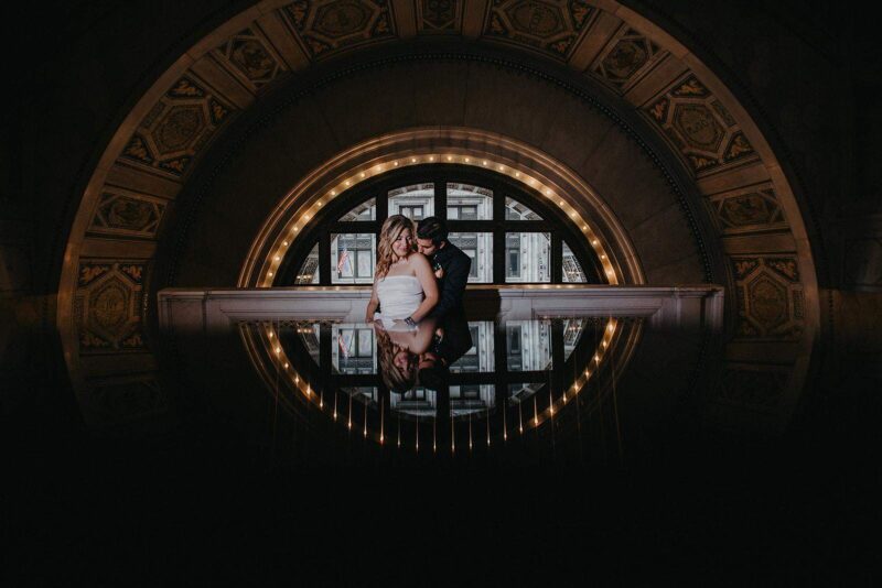 Elegant wedding couple in a luxurious historic venue with ornate architectural details.