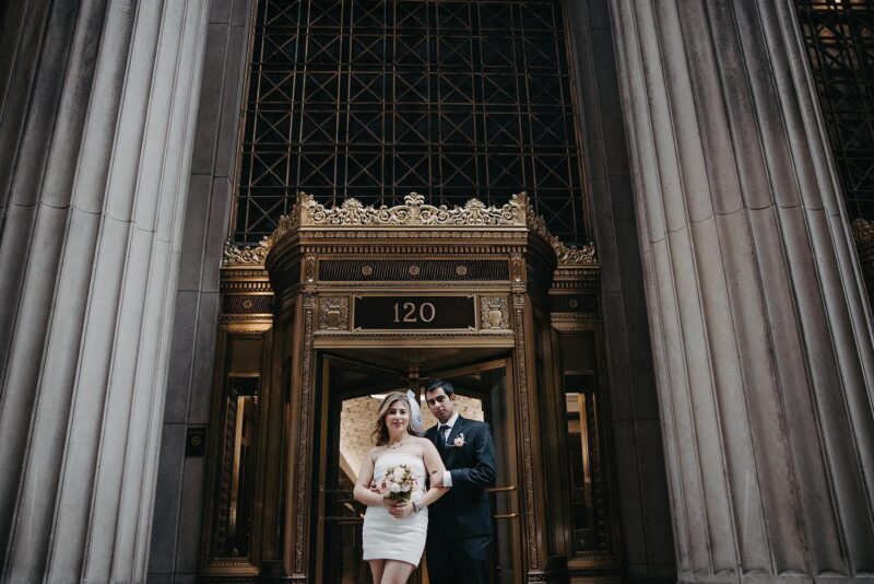 Elegant couple posing in historic luxury building with ornate entrance, perfect for high-end wedding venues.