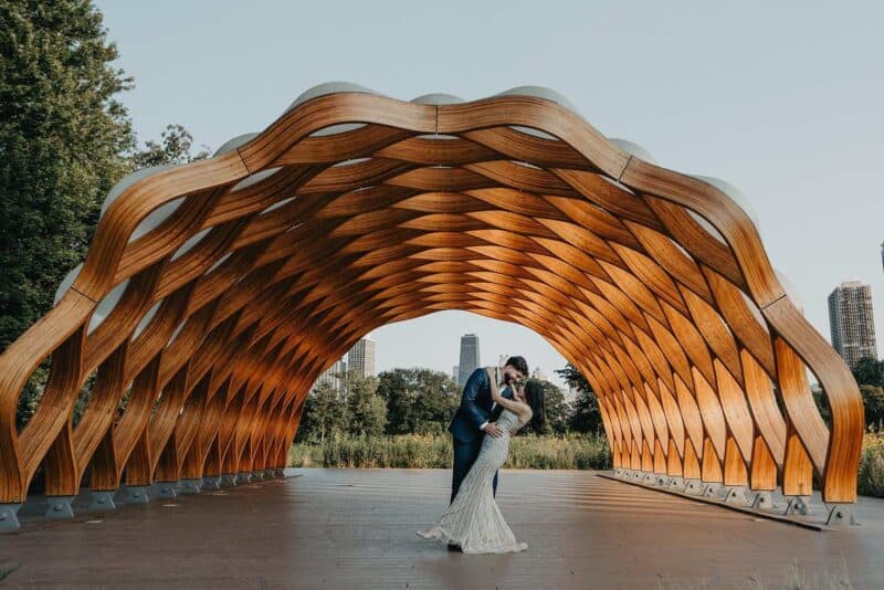 Elegant wooden wedding arch for a luxury outdoor ceremony with a couple dancing under modern skyline in the background.