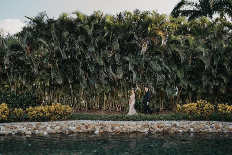 Luxurious couple posing by lush tropical plants at a high-end outdoor wedding venue.
