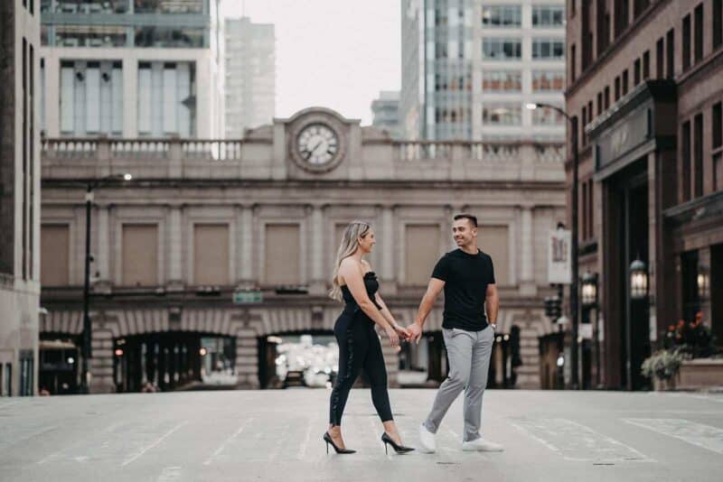 Luxurious city couple holding hands on downtown street, stylish wedding outfit, urban wedding photography.