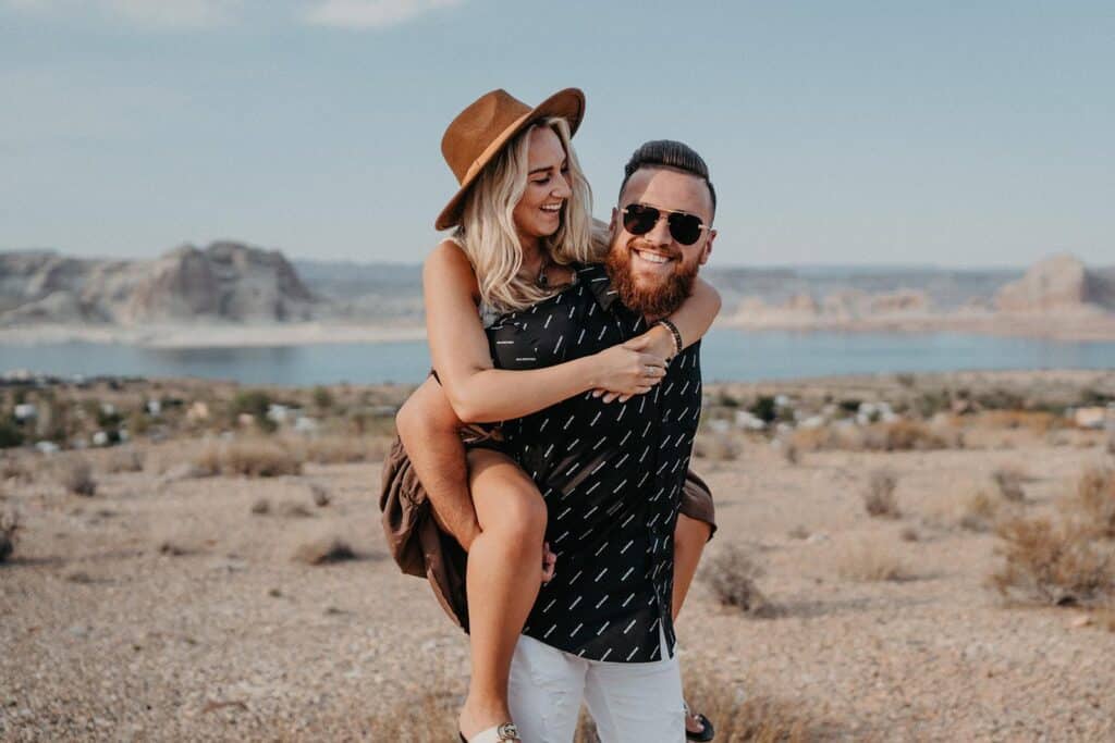 A couple enjoying a playful moment outdoors with a scenic desert and water backdrop, perfect for luxury wedding photoshoots.