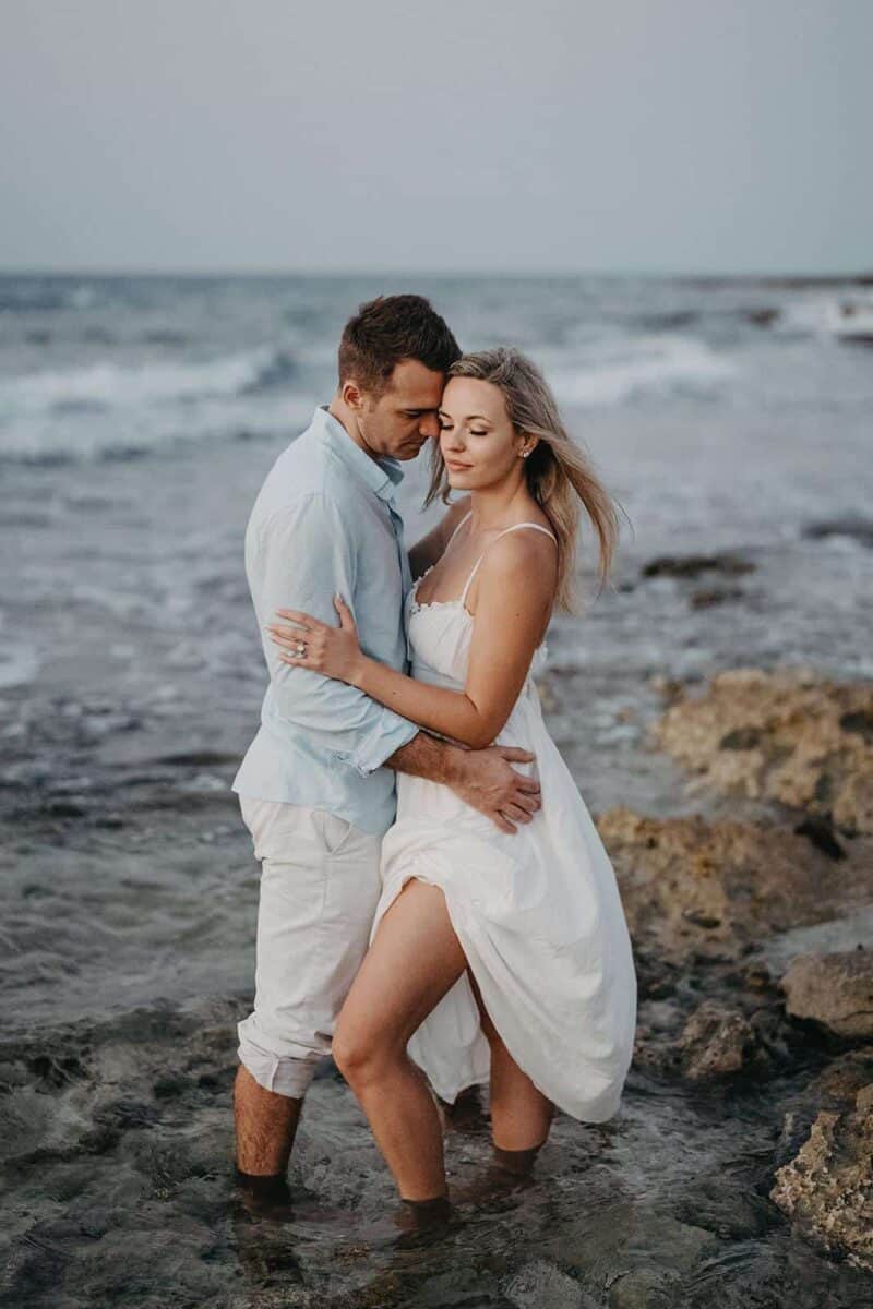 Elegant couple embracing in ocean water, romantic moment at luxury beach wedding venue, high-end destination wedding photography.
