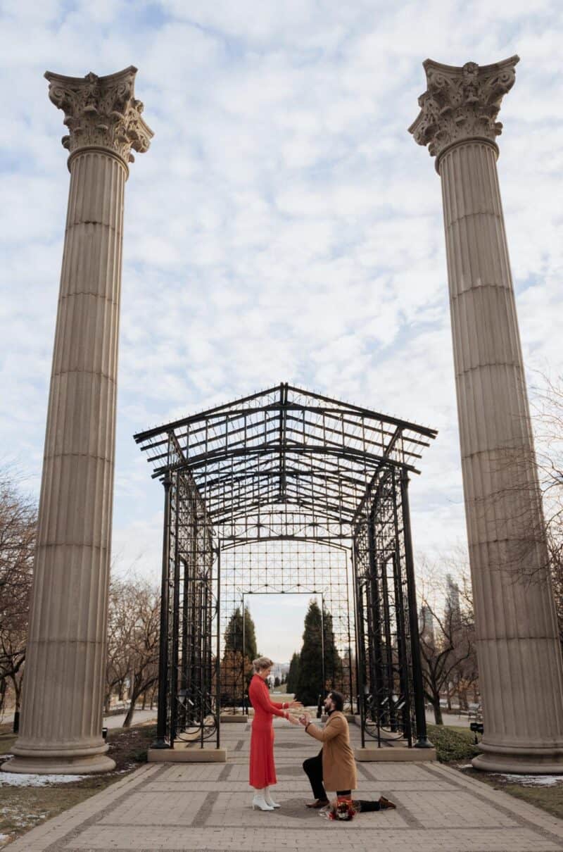 Elegant couple performing a marriage proposal in front of ancient columns at a luxurious outdoor venue.