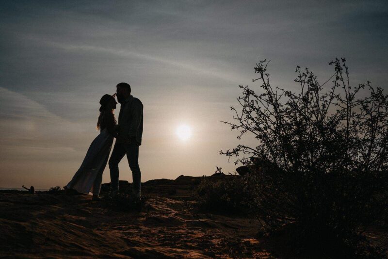 Silhouetted couple holding hands at sunset on a scenic outdoor location, perfect for luxury wedding photography and romantic wedding destination features.