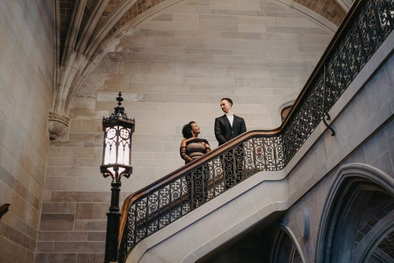 Elegant couples on grand staircase in historic luxury venue, no people, ornate ironwork, Gothic-style architecture, romantic ambiance.