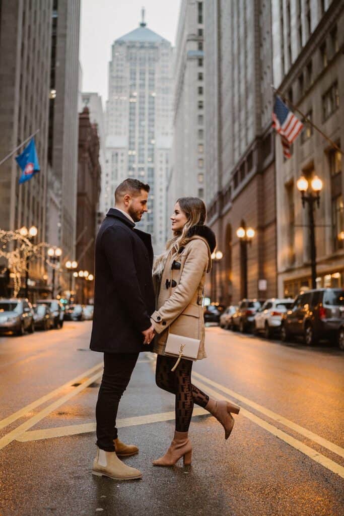 Stunning couple holding hands on city street at sunset, fashionable attire, romantic atmosphere in upscale urban setting.
