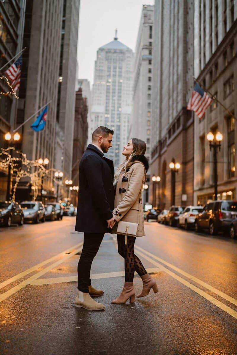 Elegant couple holding hands on a city street at dusk, showcasing luxury wedding fashion against an urban backdrop.