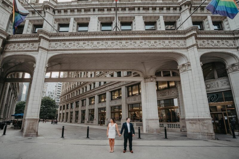 Elegant couple holding hands outside historic luxury building, perfect for high-end wedding venues.