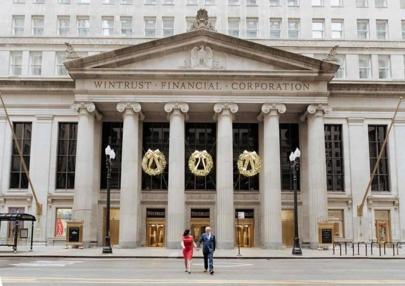 Elegant couple walking outside historic building decorated for a luxury wedding reception on city street.