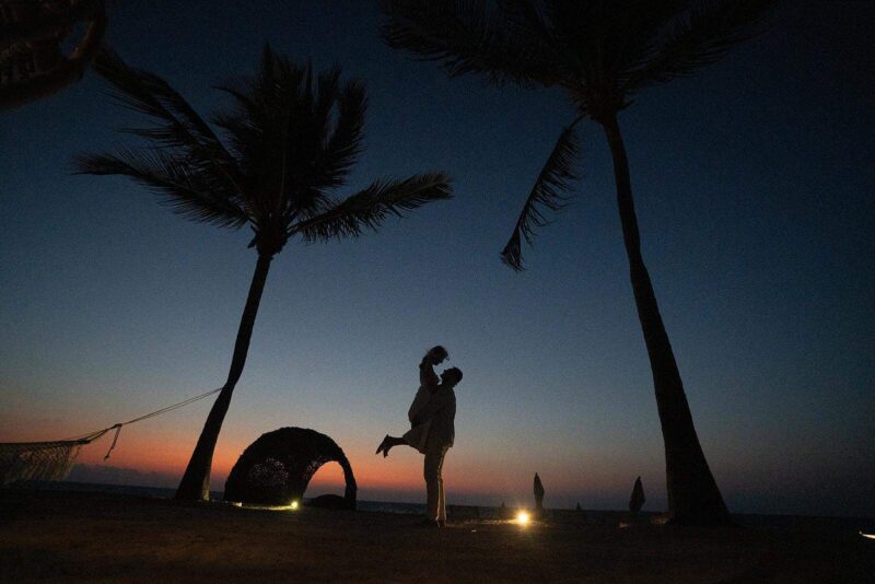 Silhouetted couple at sunset on a luxurious beach wedding venue with palm trees and romantic ambiance.