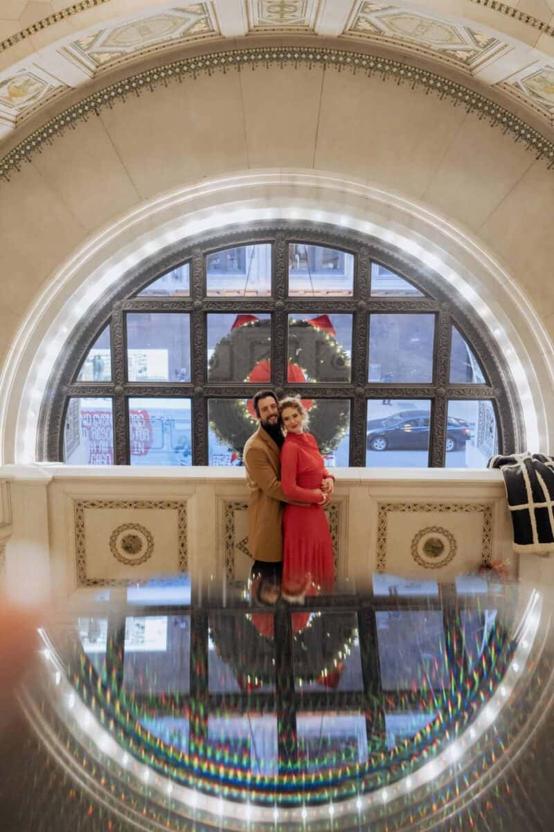 Glamorous couple celebrating Christmas inside a luxurious venue with elegant architecture and festive decor.