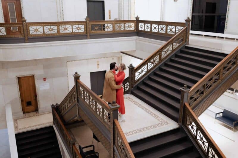 Elegant couple sharing a kiss on grand staircase in luxury hotel, perfect for high-end wedding venues.