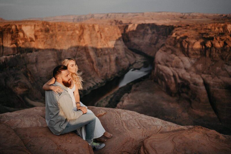 A couple sitting on the edge of a canyon during sunset, capturing a romantic moment in a stunning natural high-end setting.