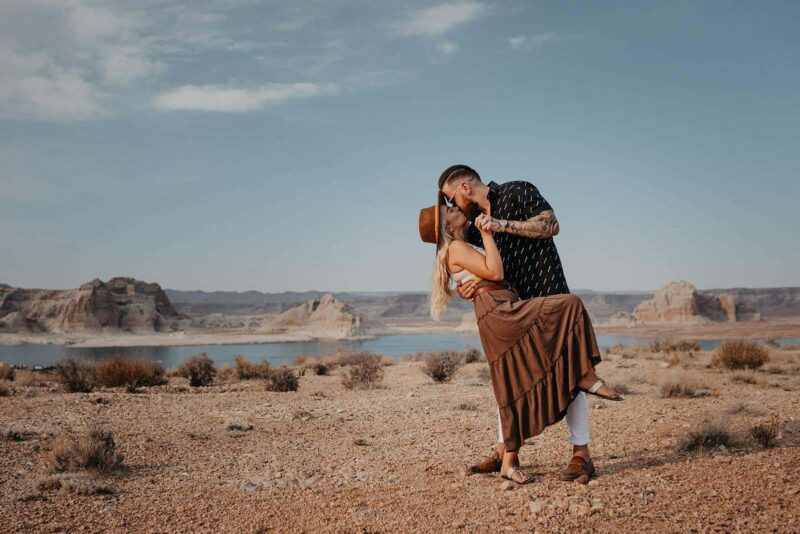 Elegant couple sharing a romantic moment in a scenic desert landscape with a lake, ideal for luxury wedding photography.
