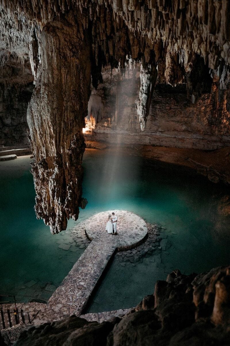Elegant cave wedding ceremony featuring a bride and groom on a stone platform surrounded by stunning stalactites and a mystical atmosphere.