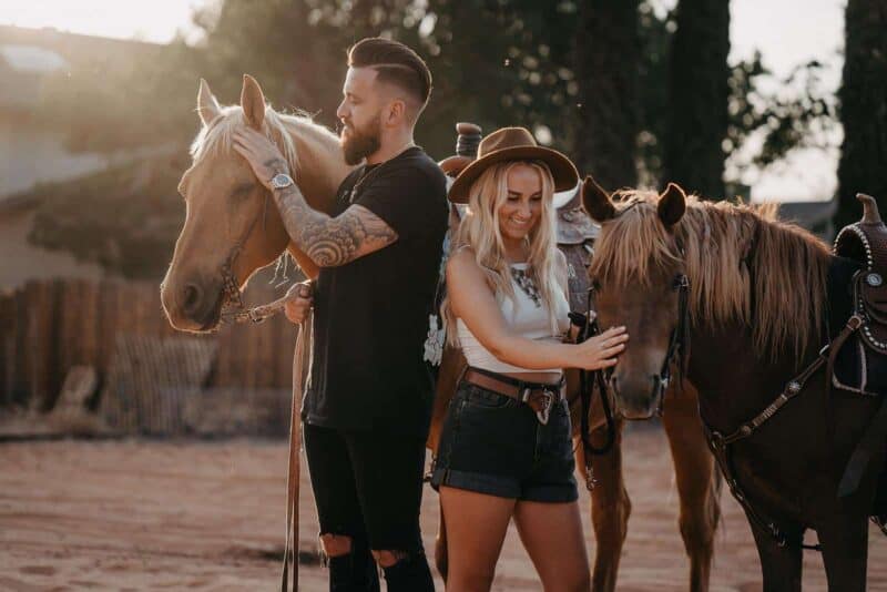 A man and woman with horses at a rustic outdoor wedding venue during sunset.