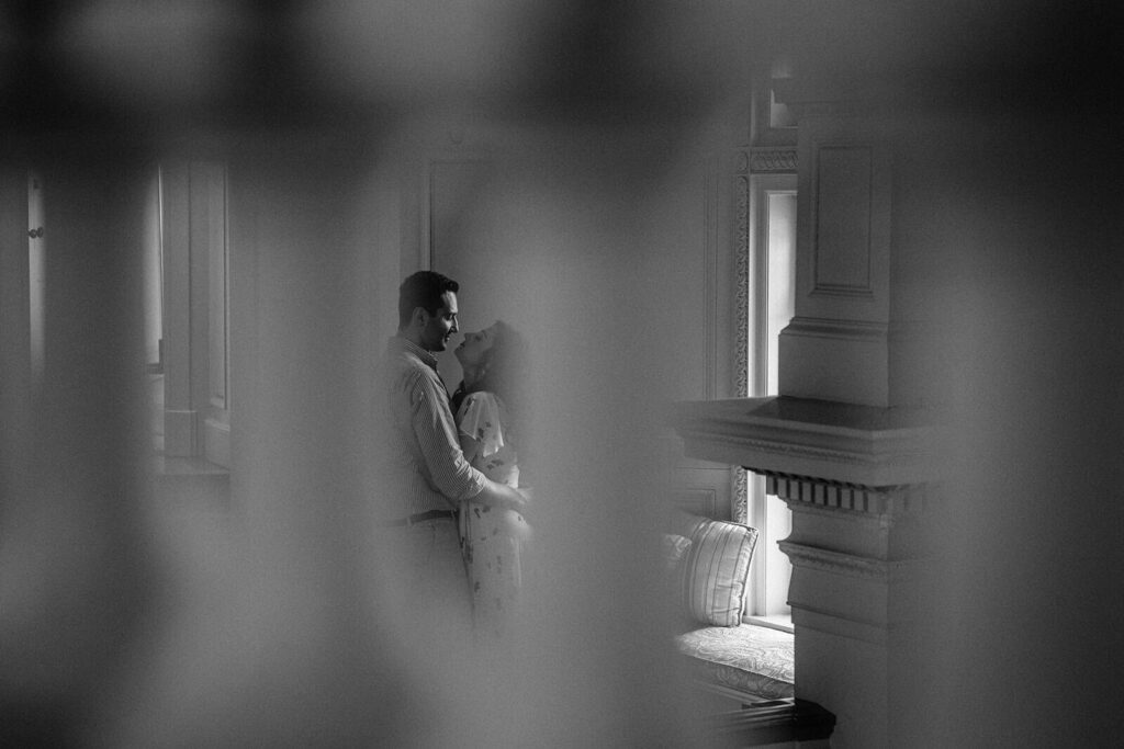 Elegant couple sharing intimate moment in luxurious wedding venue, black and white photo emphasizing romance and high-end decor.