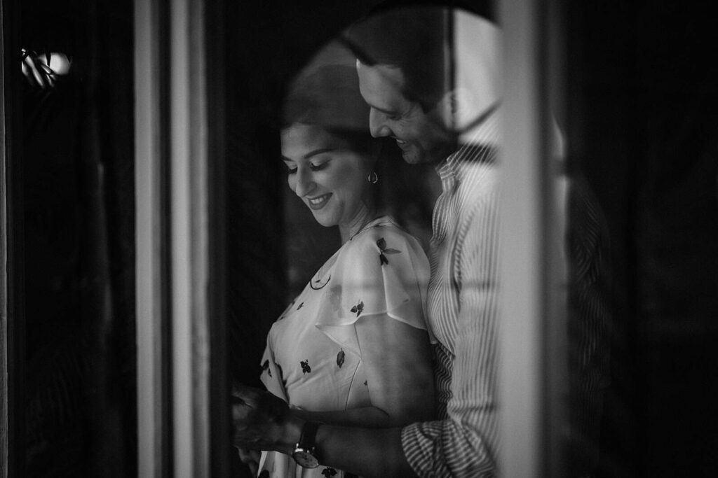 Elegant couple sharing a romantic moment behind a window, captured in black and white, ideal for luxury wedding photography.