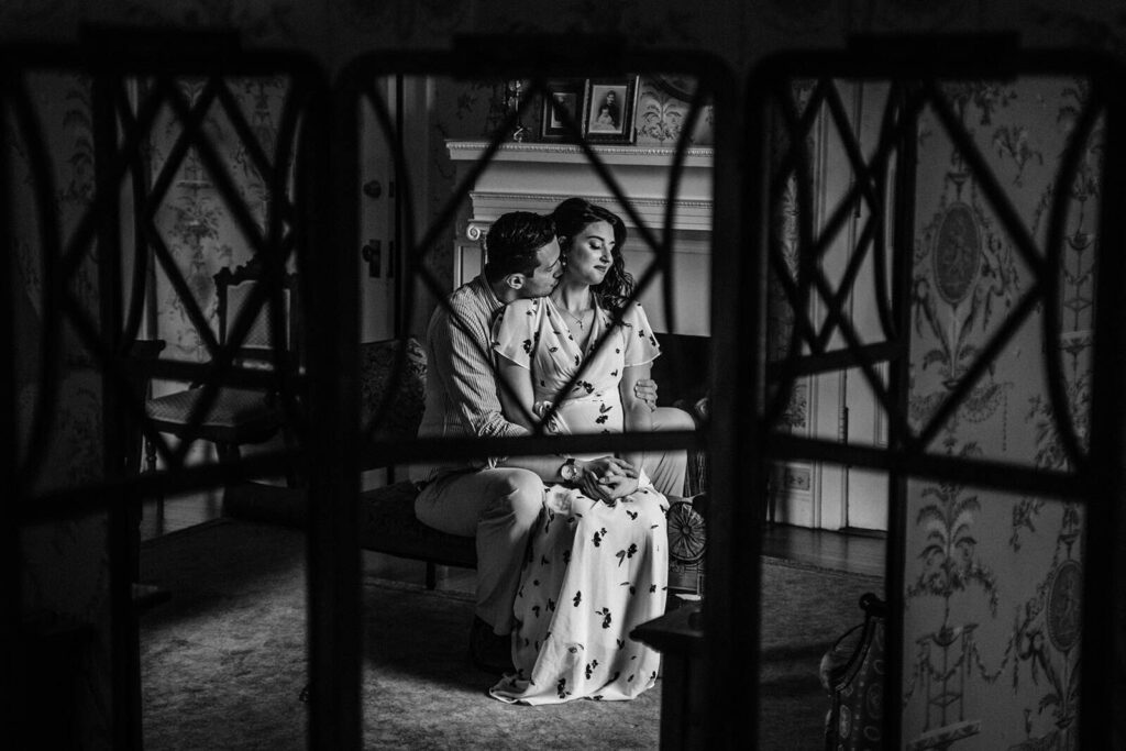 Elegant black and white photo of a loving couple sitting on a vintage sofa in a beautifully decorated high-end wedding venue.