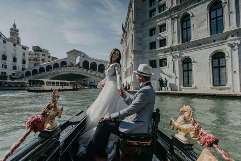Elegant wedding couple riding in a gondola along Venice canals, showcasing luxury wedding photography and scenic high-end venue views.