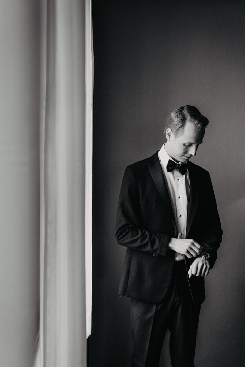 Elegant groom in black tuxedo preparing for a luxury wedding, showcasing sophistication and style at a high-end venue.