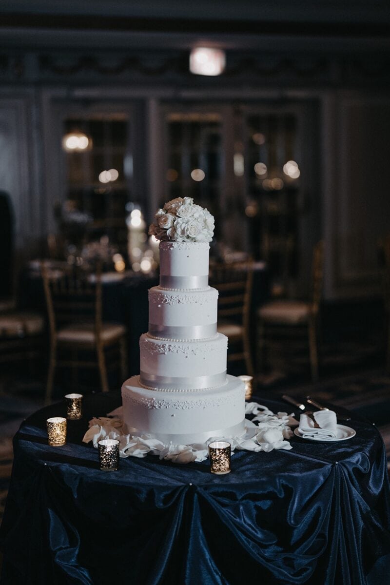 Elegant white multi-tier wedding cake with floral topper at luxury venue.