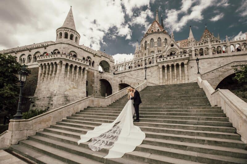 Luxury wedding couple kissing on grand staircase at fairy-tale castle.