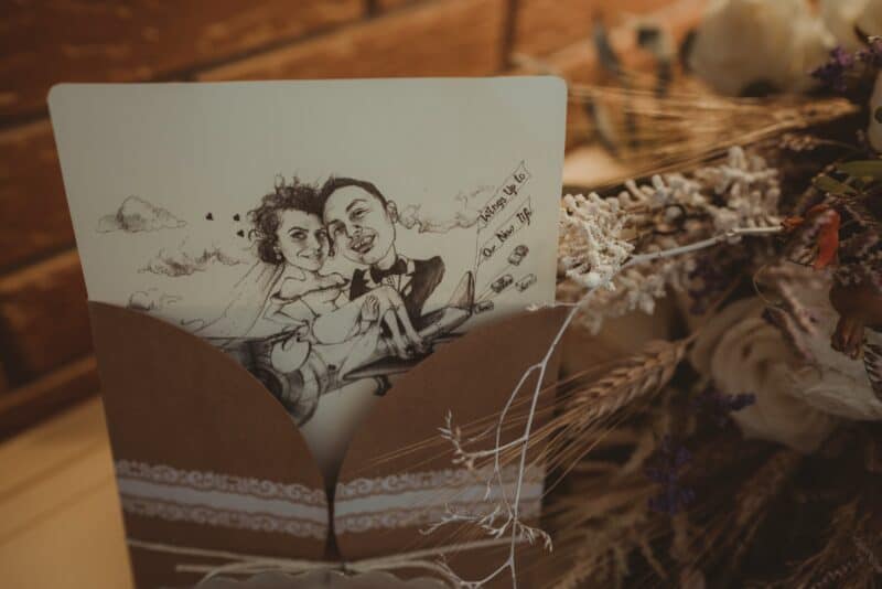 A personalized wedding caricature card sitting in a brown envelope amidst rustic floral arrangements, perfect for a luxury wedding celebration.