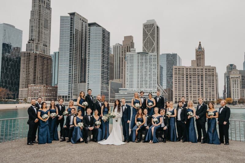 Elegant wedding party in front of Chicago skyline with high-rise architecture, bride and groom with bridal party, luxury wedding celebration, urban upscale venue, stylish couture.