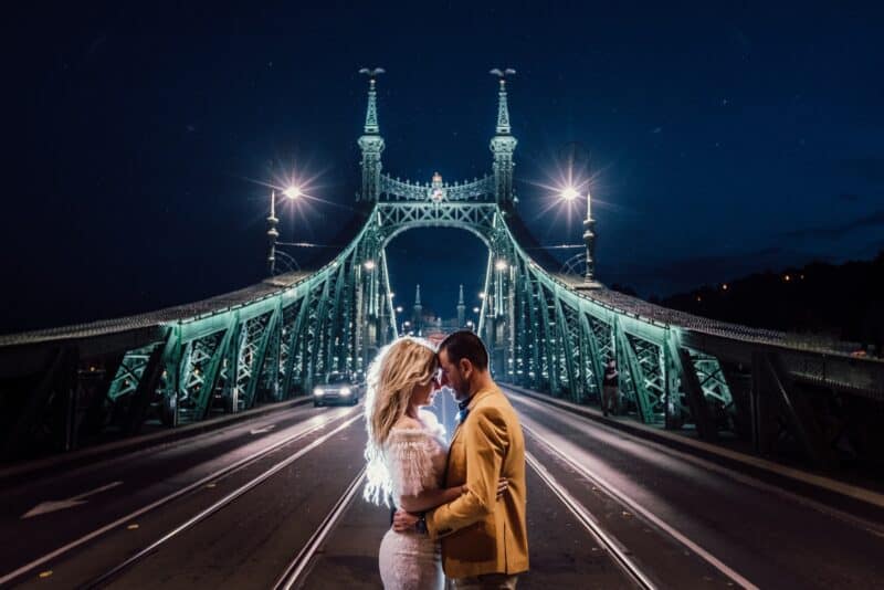 Elegant couple embracing on a illuminated bridge at night, perfect for luxury wedding photography.