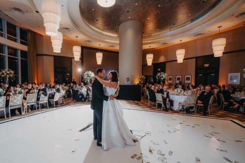 Elegant wedding dance at a luxury high-end venue, with guests seated at round tables, exquisite floral decor, and dramatic lighting accents.