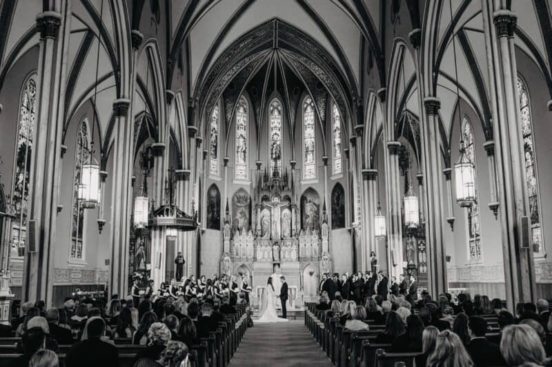 Elegant wedding ceremony inside a stunning Gothic-style church with intricate stained glass windows and ornate architecture.