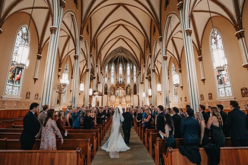 Elegant wedding ceremony inside a historic church with Gothic architecture and intricate stained glass windows.