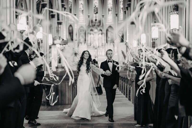 Wedding couple walking down the aisle in a luxurious church with guests celebrating.