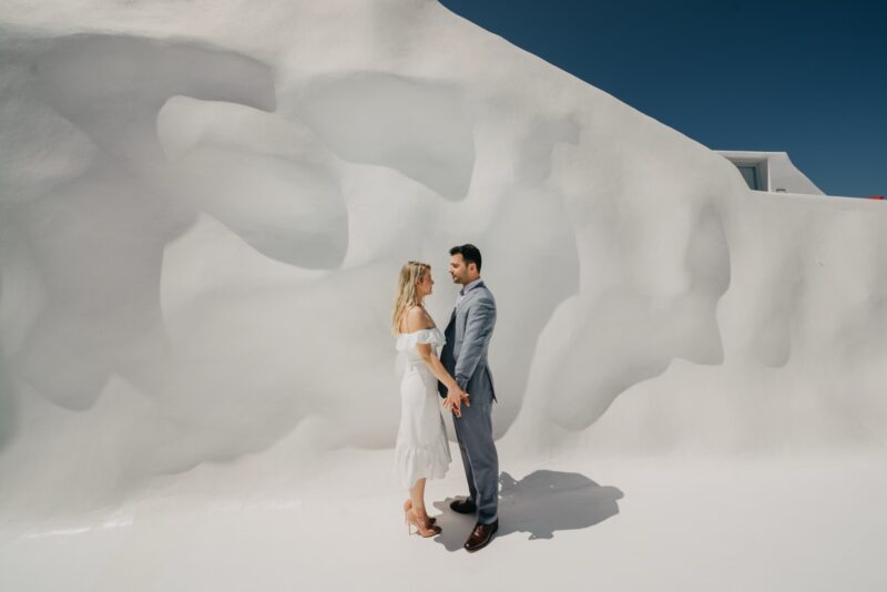 Elegant couple in wedding attire facing each other against iconic Santorini white architecture, perfect for luxury destination wedding photos.