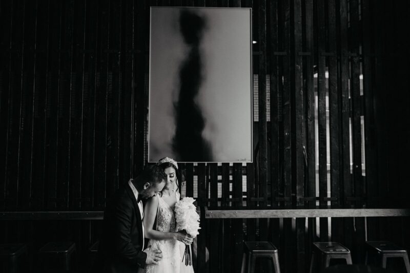 Elegant newlyweds sharing a sentimental moment in a stylish, dark-toned venue with modern decor and ambient lighting.