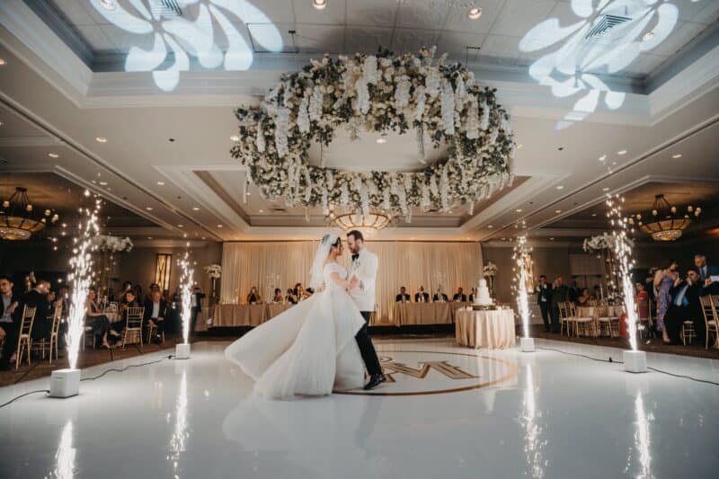 Elegant wedding dance at luxurious venue with floral chandelier and sparklers; high-end wedding reception decor.